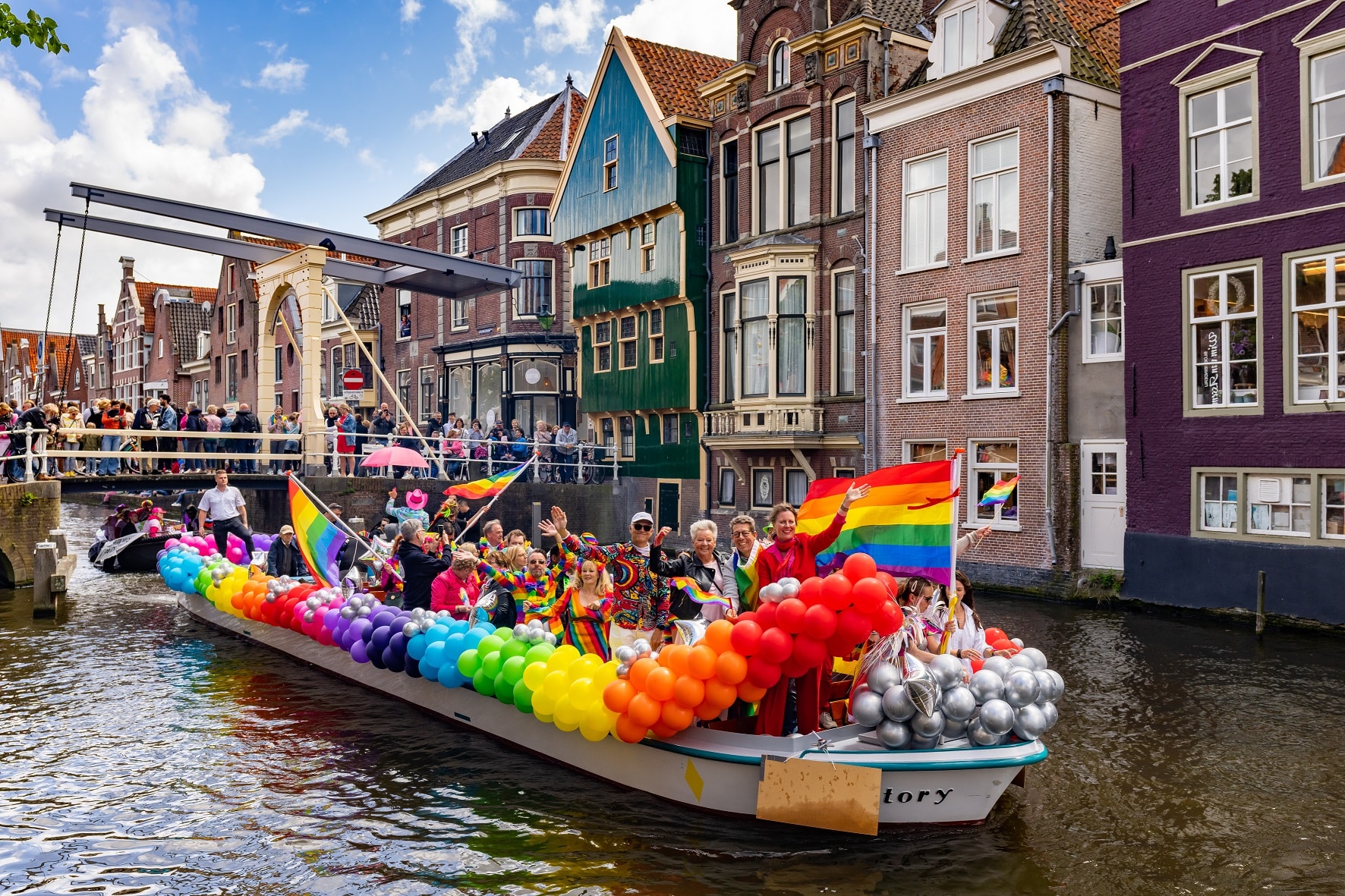 Gekleurde regenboogboot vaart door gracht Alkmaar tijdens Alkmaar Pride. Met burgemeester en wethouders voorop de boot.
