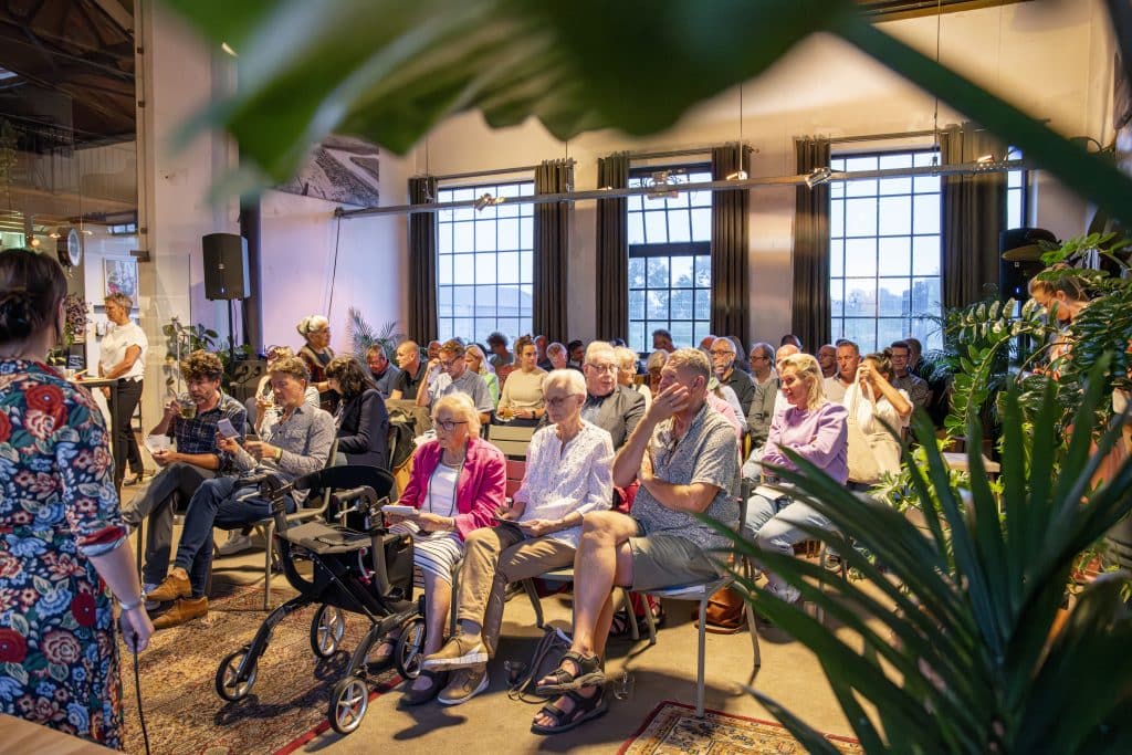 Zaal met mensen zittend op een stoel, luisterend naar een presentatie.