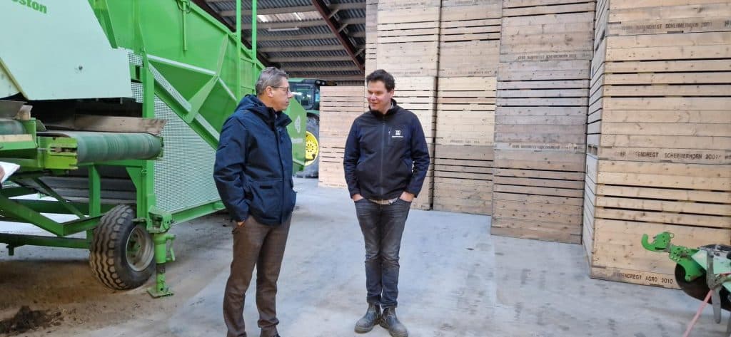 Links op de foto wethouder Robert te Beest met rechts naast hem Johan Barendregt. Daarachter kisten voor opslag van aardappelen en een landbouwmachine