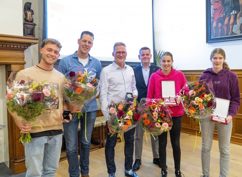 Vijf sporters staan met een bos bloemen en hun prijs in het stadhuis. Derde van rechts staat wethouder Sport Christiaan Peetoom