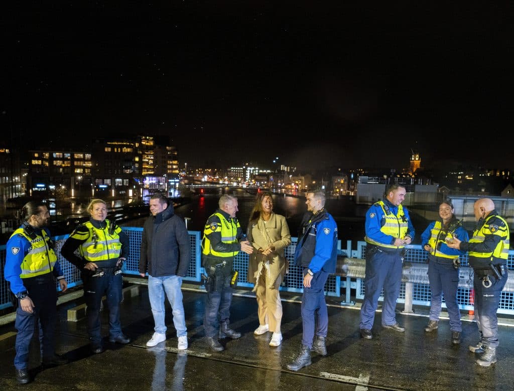 BOA's, politie en burgemeester Anja Schouten en wethouder Christiaan Peetom met elkaar in gesprek met op achtergrond lichtjes van de stad