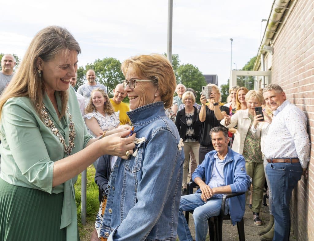 Burgemeester Anja Schouten (links op de foto) speldt een lintje op bij mevrouw Lidy Wever-Koning. Familie en bekenden kijken toe