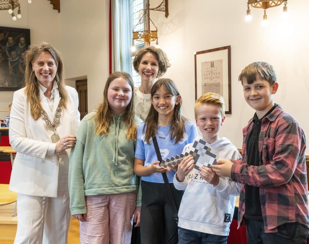 Vier leerlingen uit groep 7 van OBS Liereland krijgen de trofee voor hun winnende Minecraft-ontwerp van burgemeester Anja Schouten en projectleider Meis de Jongh