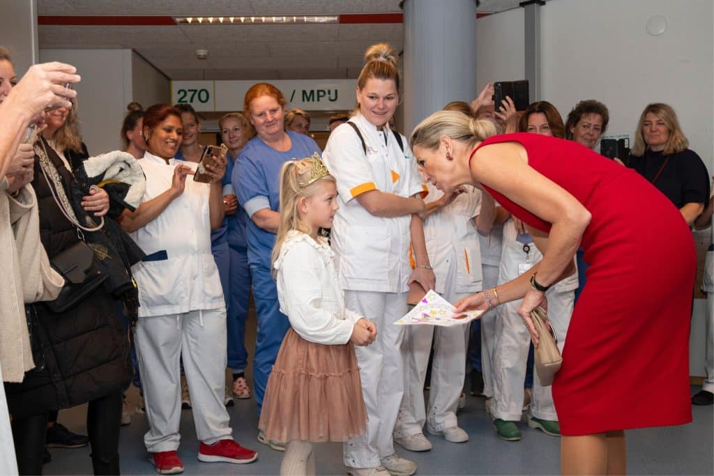 Koningin Máxima ontvangt een kleurplaat van een jonge vrouw en spreekt met haar in het Noordwestziekenhuis. Er zijn verschillende gezondheidswerkers om hem heen.