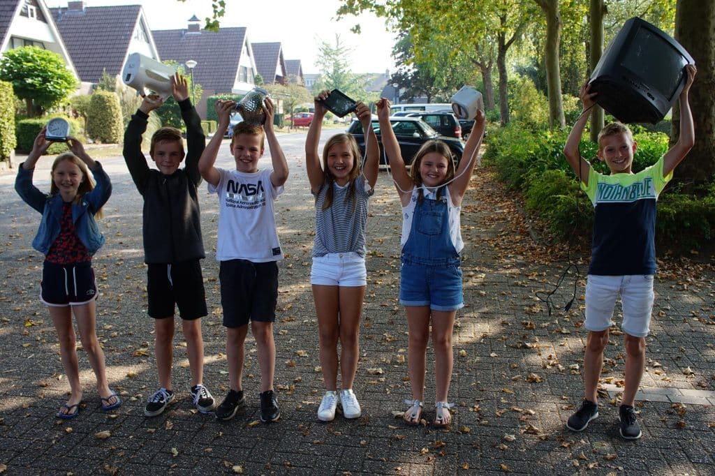 6 kinderen staan in een straat en houden elektronisch afval boven hun hoofd.