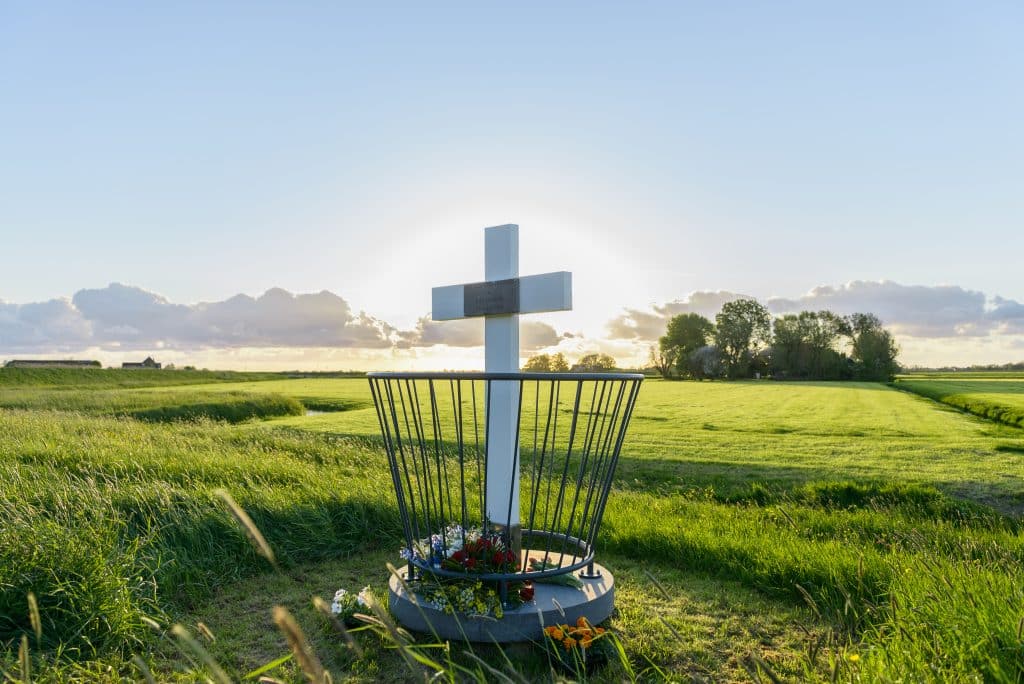 Herdenkingskruis Noordeindermeerdijk. Foto van het herdenkingskruis in het weidse landschap met erachter de zon.