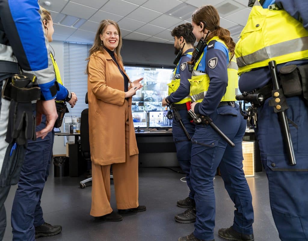 Burgemeester Anja Schouten staat naast een groepje BOA's in uniform met op de achtergrond een groot scherm.