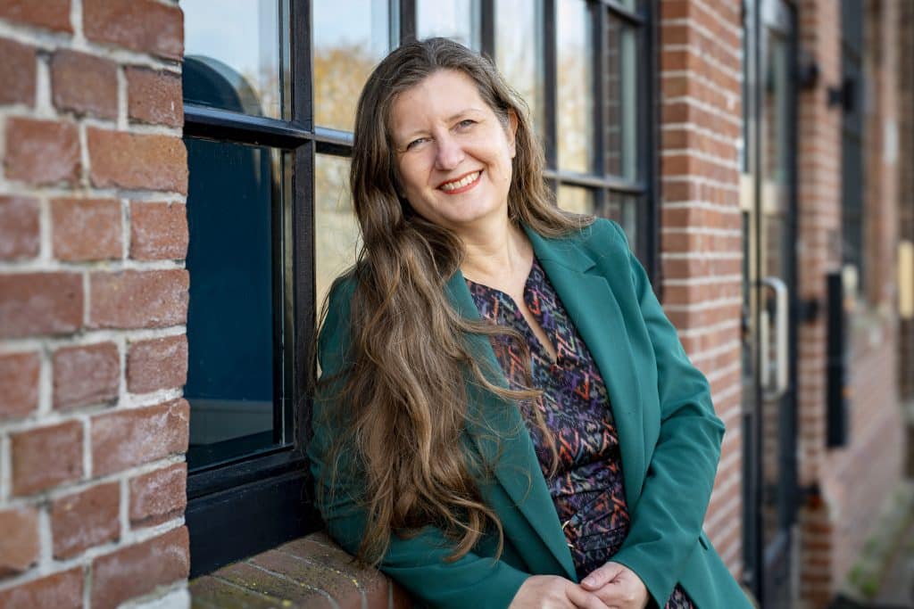 Vrouw die tegen de buitenkant van een kozijn aanleunt. Het is de ombudsman van de gemeente Alkmaar, mevrouw Anneke Wezel