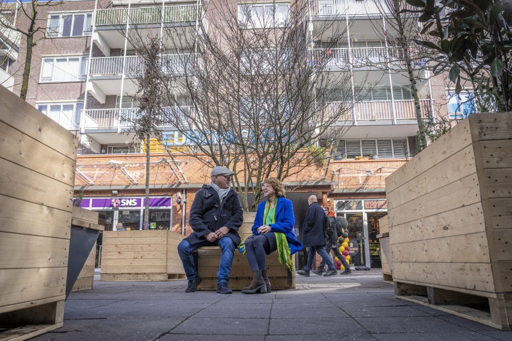 Man en vrouw zitten op bankje bij een van de mobiele bakken met bomen en groen erin