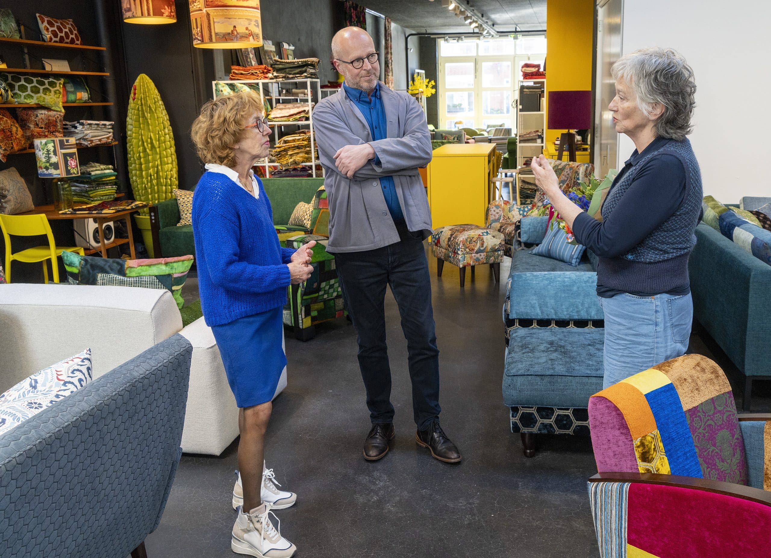 Drie mensen in een showroom voor meubels. De meubels zijn kleurrijk. De drie mensen zijn in gesprek met elkaar