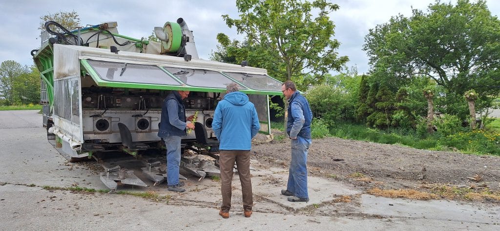 Drie mannen staan bij een oogstmachine voor spruitjes