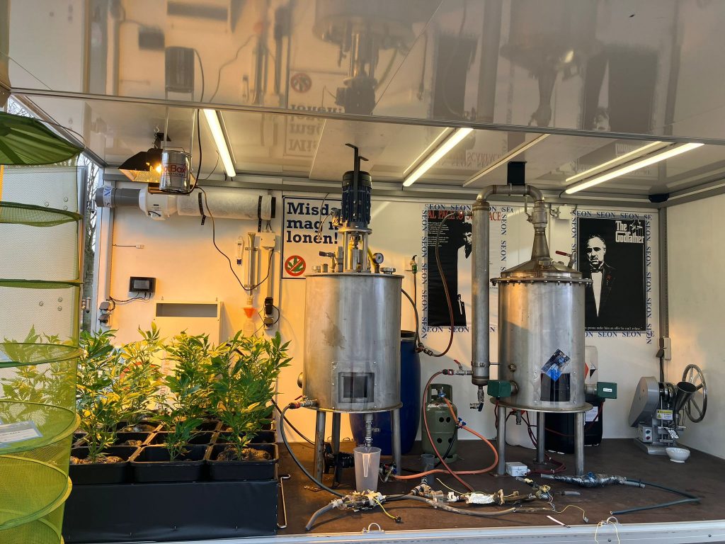 Binnenkant van de Speedmobiel met een nagebouwd drugslab en hennepkwekerij, inclusief ketels, jerrycans en hennepplanten.