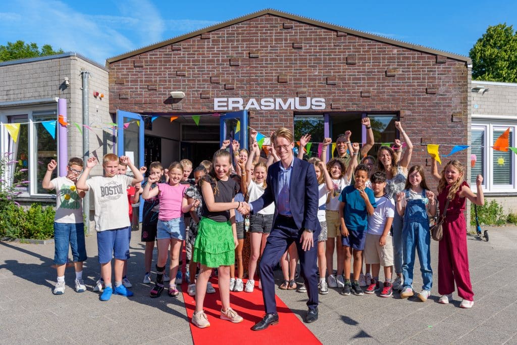 Man geeft hand aan meisje. Op de achtergrond juichende kinderen en een gebouw met ''Erasmus'' erop