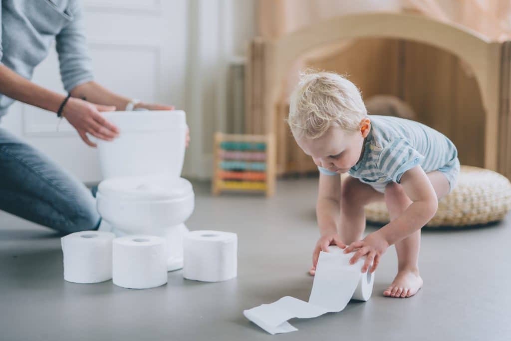 Peuter met een wc-rol naast een stapel wc-rollen en een potje
