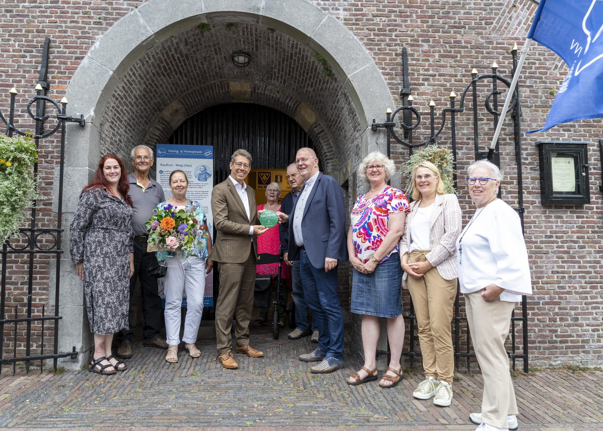 Een groepje van 10 mensen staat voor een gebouw. In het midden staat wethouder Robert te Beest die de toeristische Michelin-ster overhandigt aan Bob Kiel, voorzitter van VVV De Rijp en Land van Leeghwater.