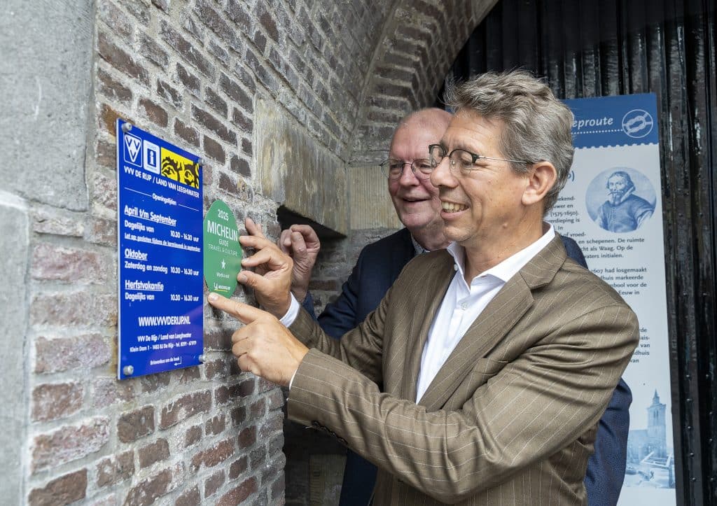 Wethouder Robert te Beest en Bob Kiel, voorzitter van VVV De Rijp en Land van Leeghwater, bevestigen de toeristische Michelin-ster op de muur van het VVV-gebouw in De Rijp.