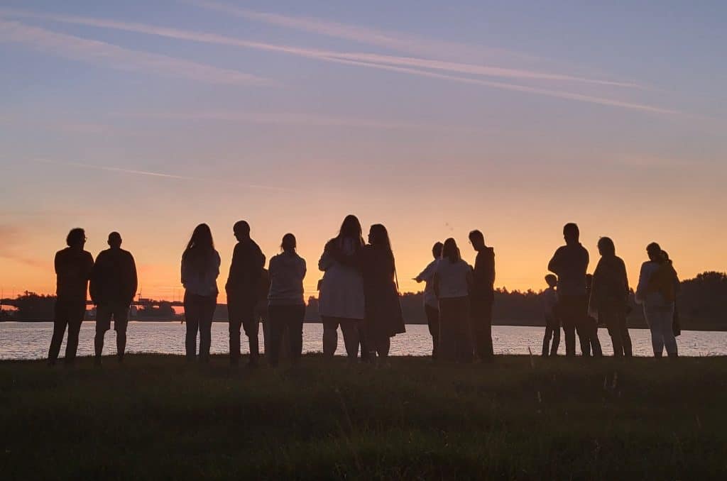 Foto van mensen die aan de waterkant staan bij zonsopgang