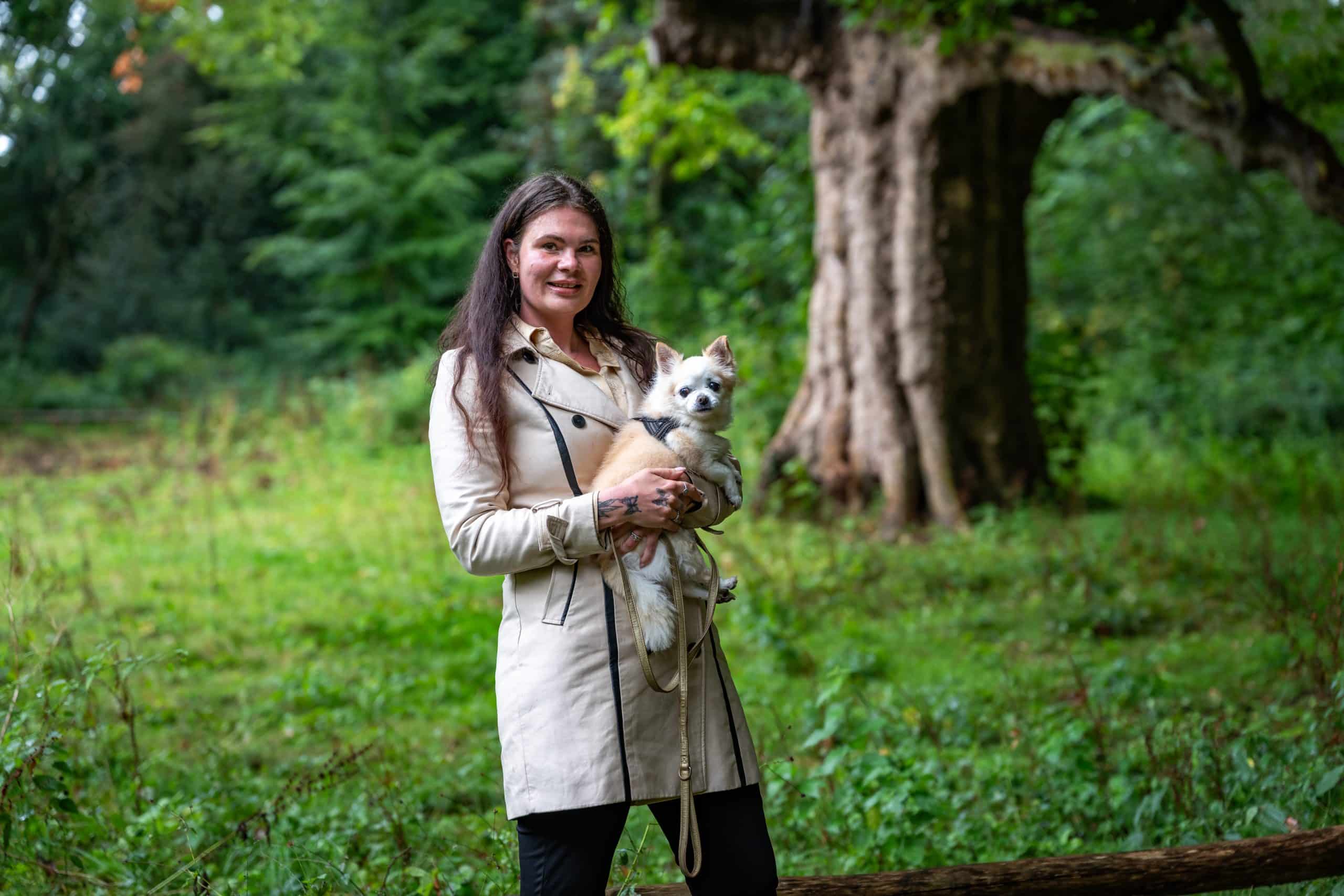 Anne heeft haar hondje opgetild in haar armen en staat in de Hout