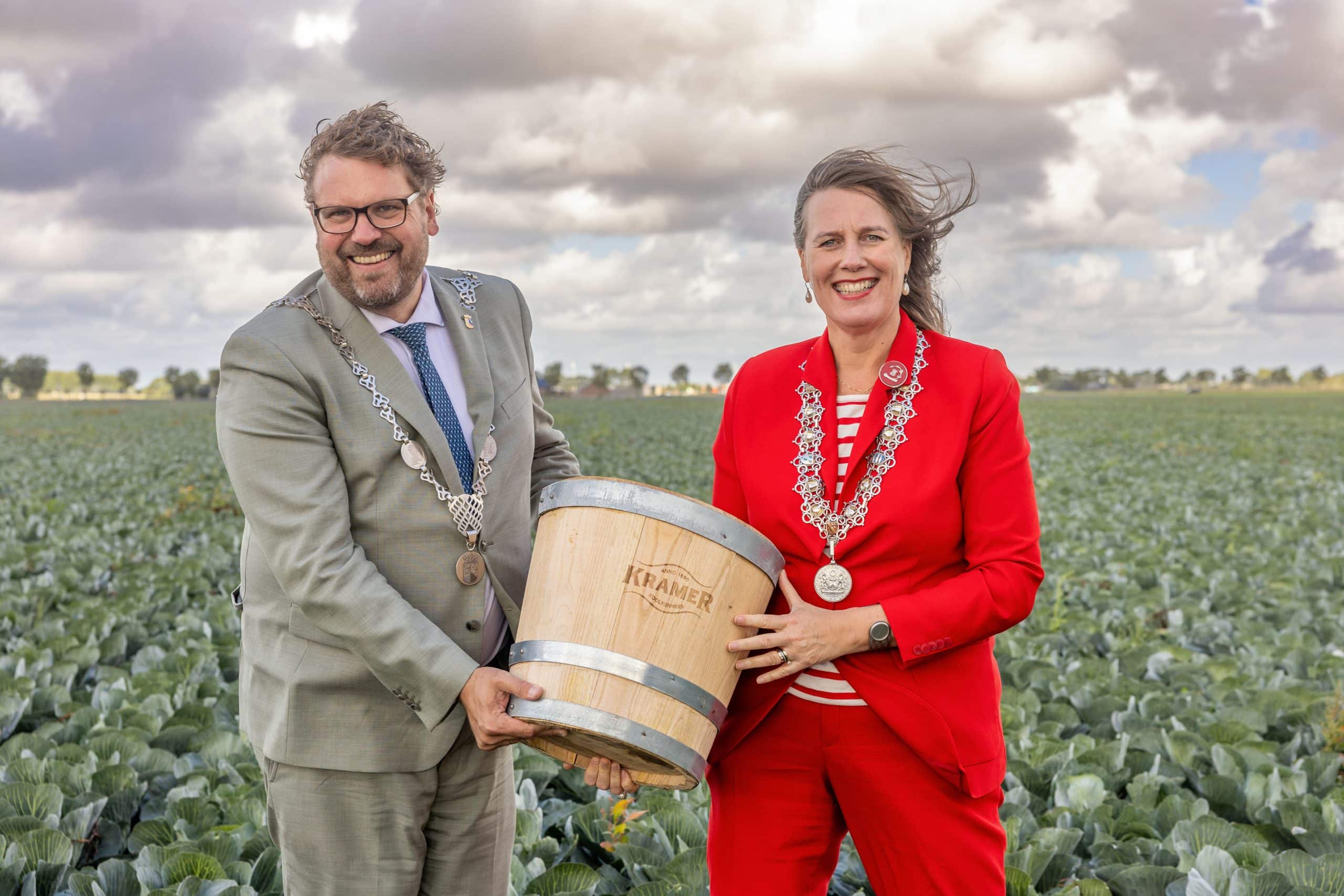 Burgemeester van Dijk en Waard en van Alkmaar staan in een kolenveld met een vaatje zuurkool die zij samen vasthouden