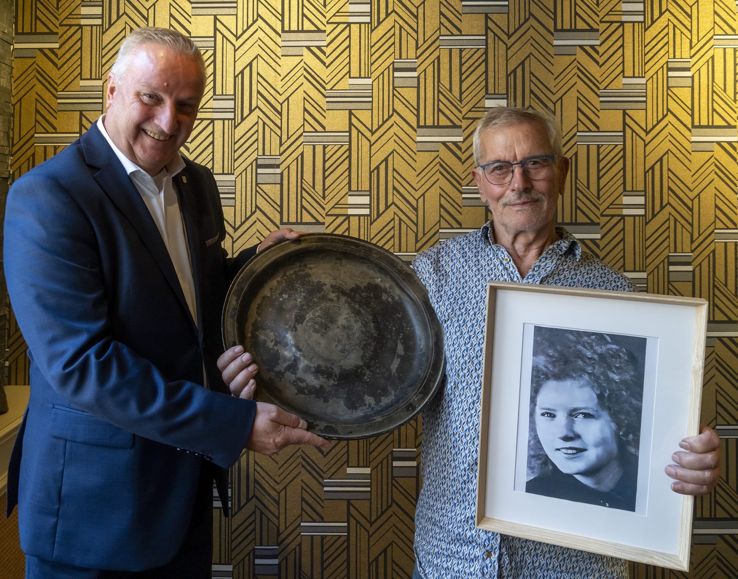 Man schenkt schaal aan wethouder. Hij heeft de foto van zijn vrouw, de vinder ervan, vast 