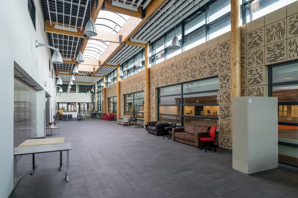 Brede gang in gebouw De Letterbak met langs kant banken en stoelen.
