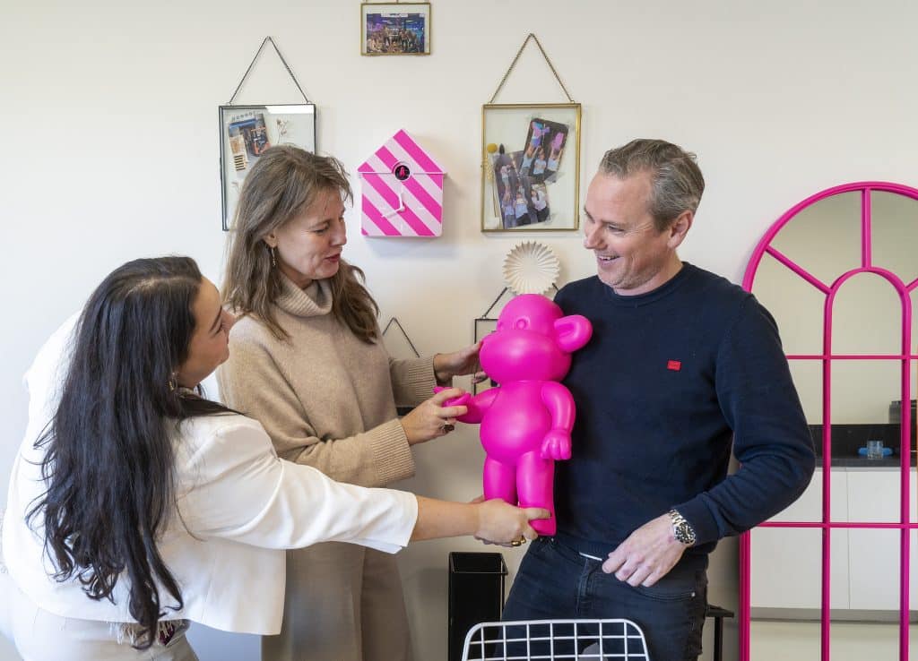 Twee vrouwen en een man houden een roze beeld vast bij een man