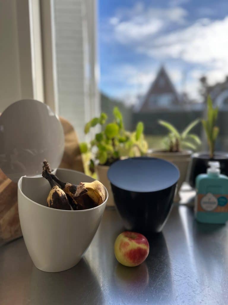 Een zwart en wit gft-keukenbakje op het aanrecht. In het witte bakje zitten bananenschillen. Op het aanrecht ligt een appel. 