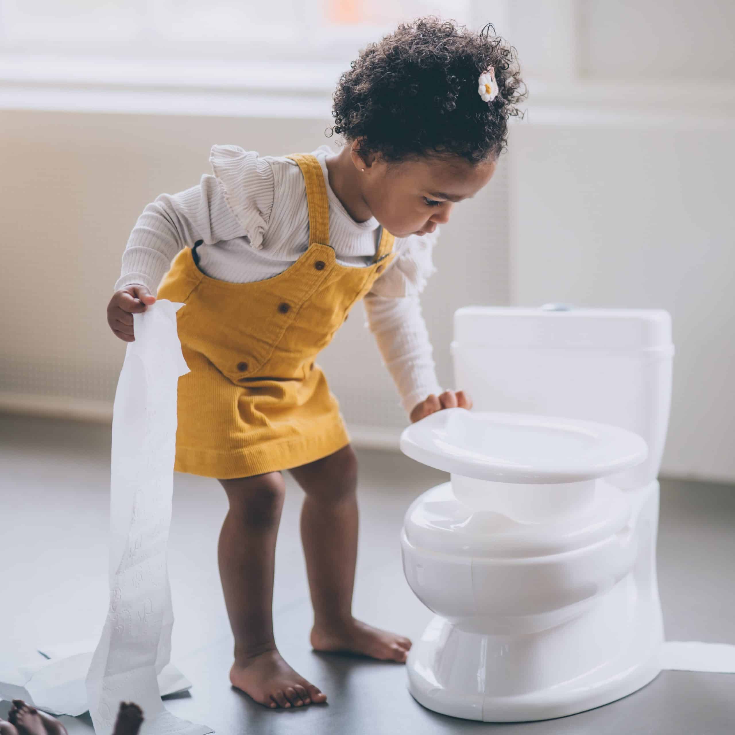 Kind met wc papier in de ene hand. Het houdt een potje vast in de vorm van een echte wc.