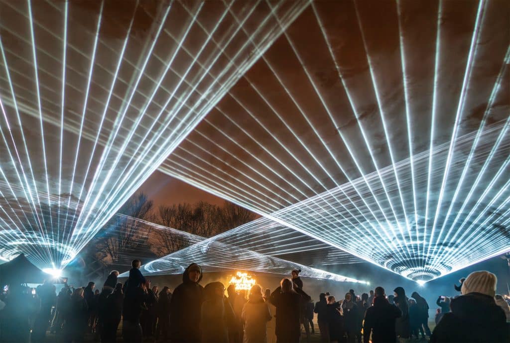 Een lasershow met meerdere lichtstralen in de lucht met op de voorgrond mensen die kijken naar de show