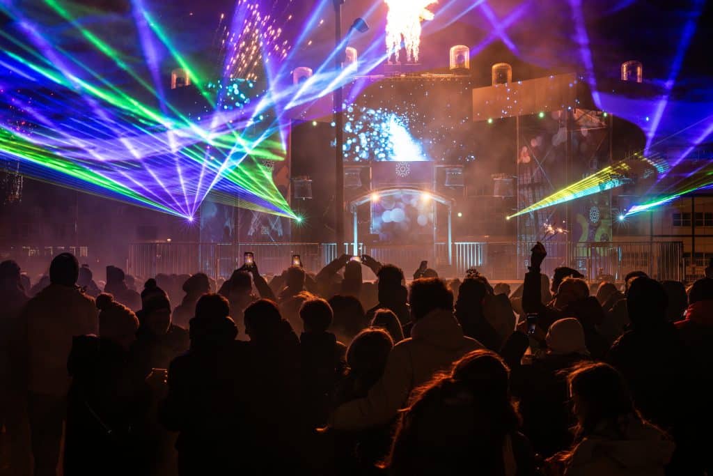 Een groep mensen kijkt naar een podium met lasers en vuurwerk
