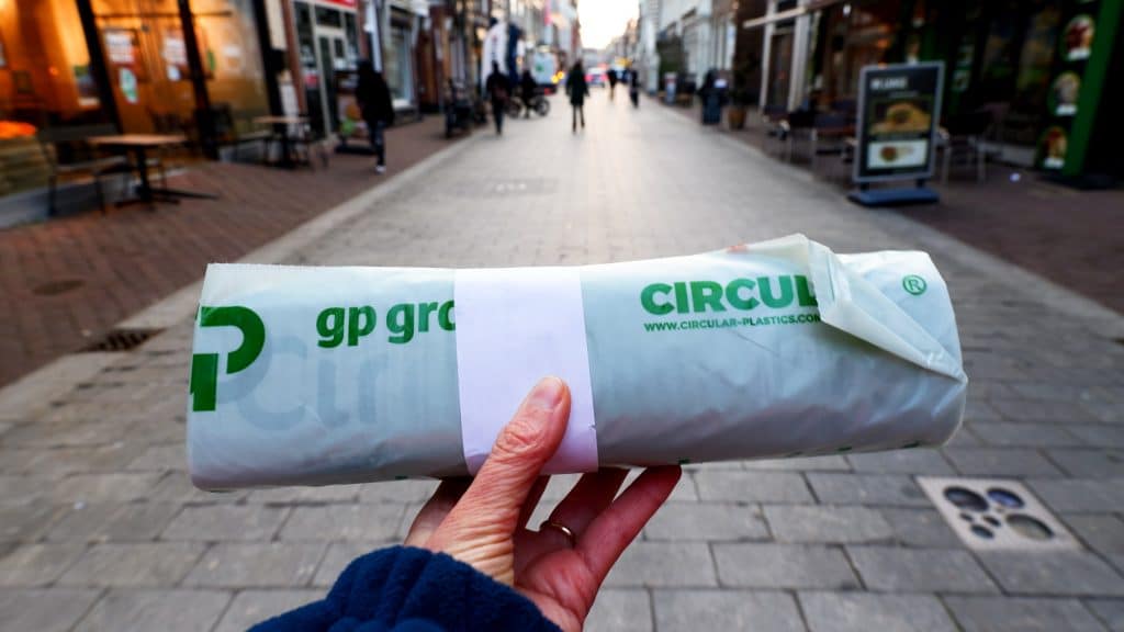 Een hand die een rol foliezakken vasthoudt. Op de achtergrond winkelstraat de Langestraat in Alkmaar.