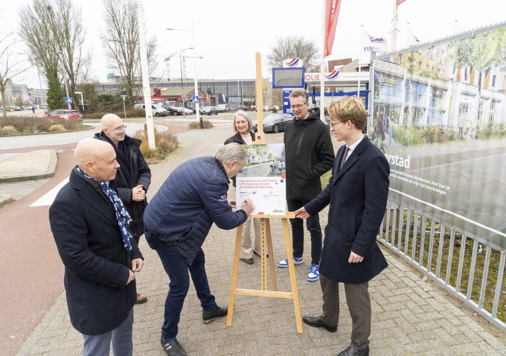 Wethouder Lars Ruiter en Richard Fieten ondertekenen de overdracht van het gaspunt in Overstad, terwijl andere betrokkenen toekijken.