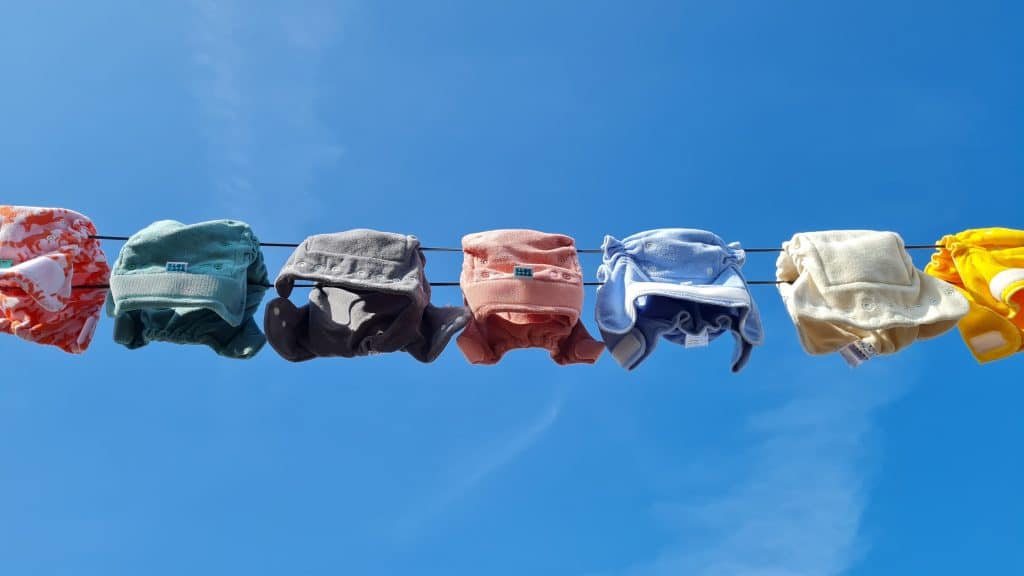 Gekleurde wasbare luiers aan een waslijn met blauwe lucht op de achtergrond.