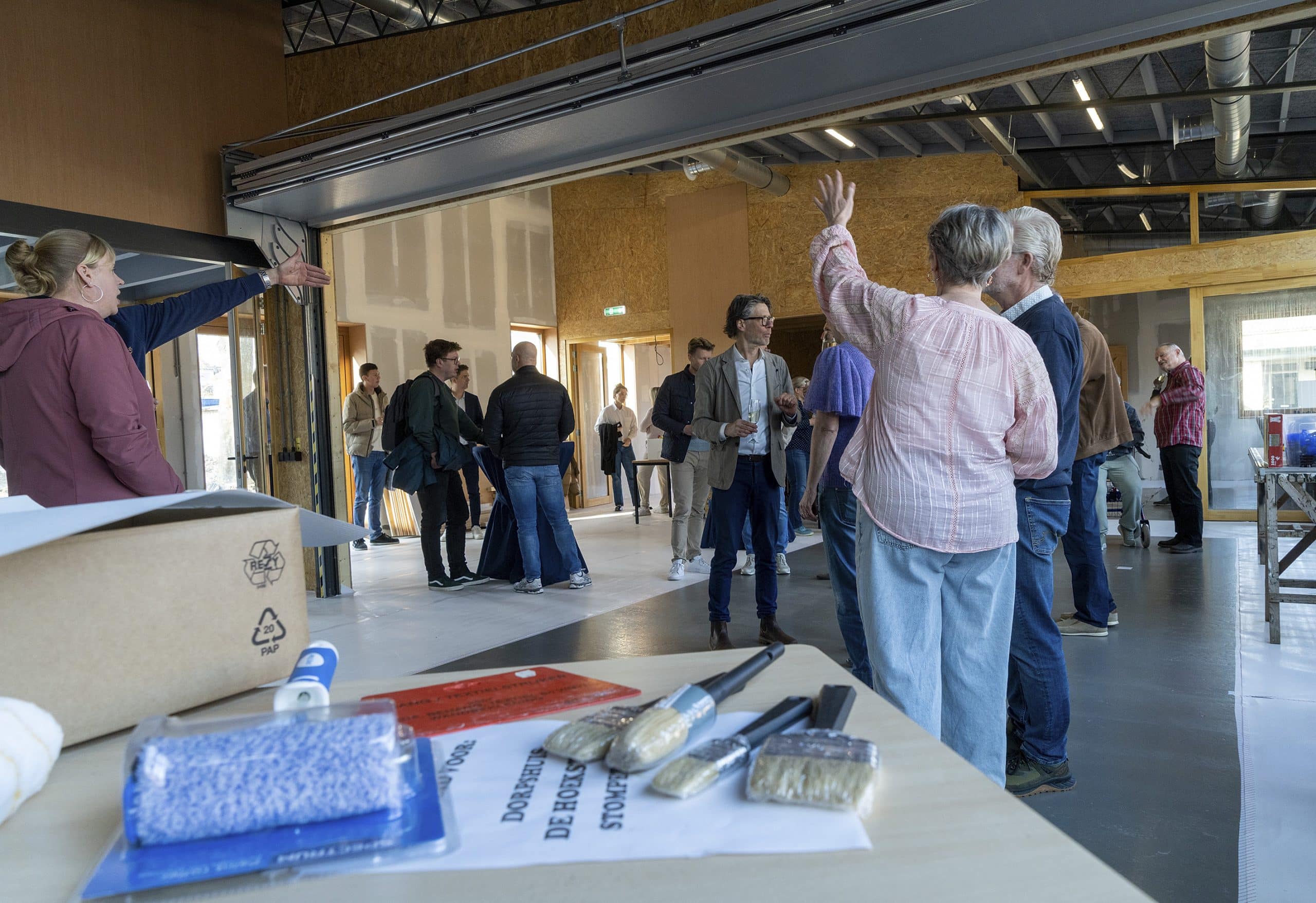 Foto van het buurthuis van binnen. Belangstellenden staan het pand van binnen te bekijken en zijn in gesprek. 
