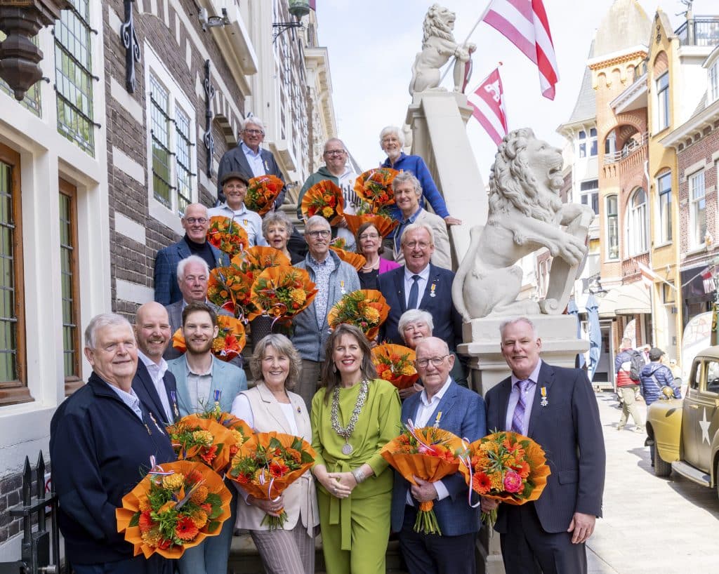 Op een trap staan alle mensen met een lintje. daar tussen staat ook de burgemeester. De trap is bij het Stadhuis van Alkmaar.