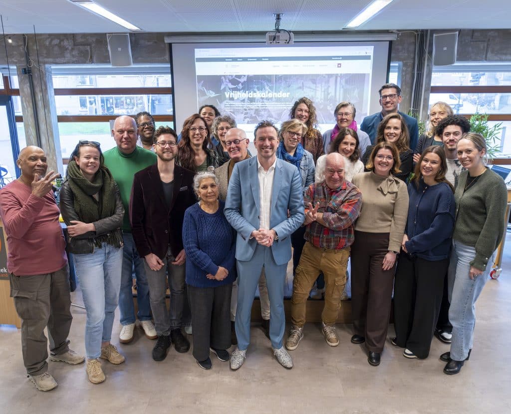 Een groep van ongeveer twintig mensen uit de culturele sector en inclusiepartners staat samen op de foto in een ruimte, met op de achtergrond een scherm met de Vrijheidskalender.